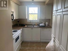 St. Catharines (Glendale/Glenridge) fourplex for rent - A kitchen with white cabinets and appliances, a window above the sink, and a bag on the floor.