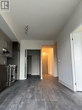 Toronto (Don Valley Village) condo for rent - A spacious, empty room with a kitchen area to the left and a doorway leading to another room.