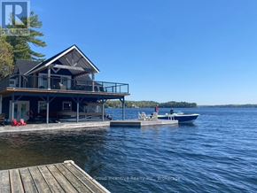 Muskoka Lakes (Medora) house for rent - A house with a deck overlooking a body of water with a boat and a person on it.