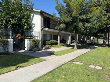 Anaheim apartment for rent - A white building with a black fence and a green lawn in front.