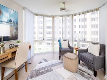 Arlington apartment for rent - A living room with a white chair, a grey couch, and a wooden desk with a lamp on it.