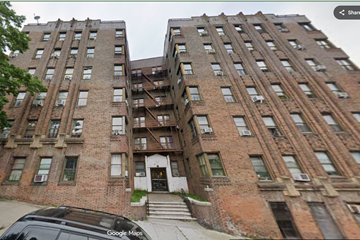 Bronx apartment for rent - A street view of a large brick building with a car parked in front.