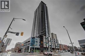 Kitchener condo for rent - A tall building with a glass facade stands in front of a street with traffic lights.