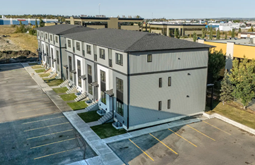 Red Deer County apartment for rent - A large grey building with a parking lot in front.