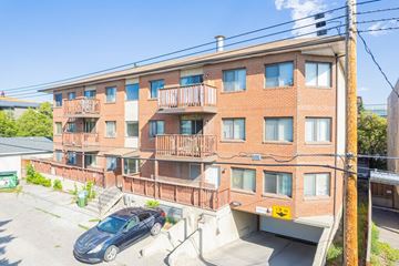 Calgary apartment for rent - A grey car is parked in the driveway of a red brick apartment building.