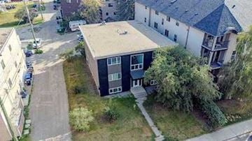 Calgary apartment for rent - A black and white building with a green lawn in front.