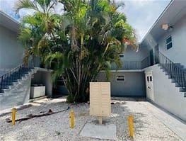 Miami apartment for rent - A concrete structure is placed in the middle of a courtyard with a tree and two buildings in the background.