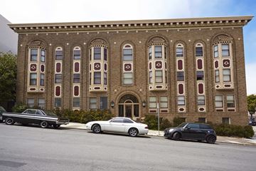 San Francisco apartment for rent - A black car is parked in front of a brick building with arched windows.