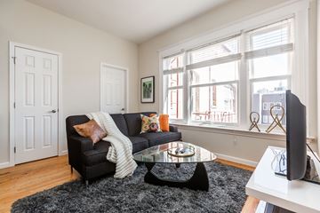 San Francisco apartment for rent - A black couch with a white blanket and pillows sits in a living room with a glass coffee table in front of it.