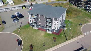 Moncton apartment for rent - A large building with a grey roof and a parking lot in front.