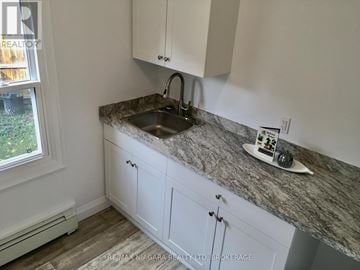 St. Catharines (Downtown) house for rent - A kitchen with a granite countertop and white cabinets.