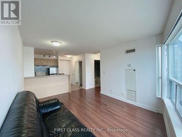 Toronto (Woburn) condo for rent - A black leather couch sits in a spacious living room with wood flooring and white walls.