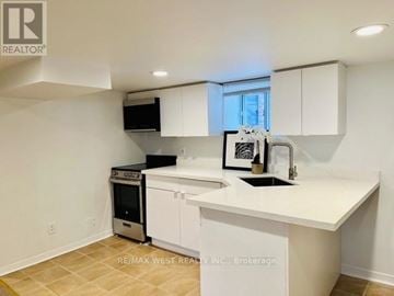 Toronto (High Park North) house for rent - A white kitchen with a black fridge and a black microwave.