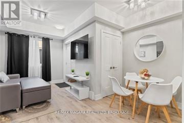 Niagara Falls (Arad/Fallsview) townhouse for rent - A modern living room with a grey sofa, a white dining table with chairs, and a television.