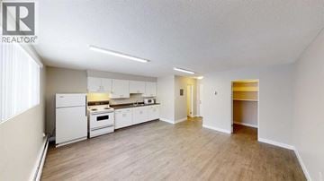 For rent in Grande Prairie - A well-lit, spacious kitchen with white appliances and wooden flooring.