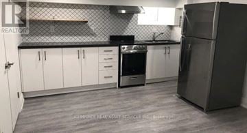 Toronto (Trinity-Bellwoods) house for rent - A kitchen with white cabinets and a black stove top oven.