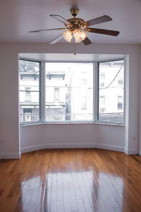 Jersey City apartment for rent - an empty living room with a large window and a ceiling fan