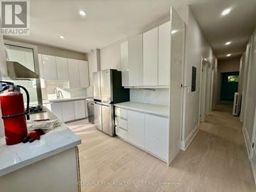 Toronto (Trinity-Bellwoods) house for rent - A modern kitchen with white cabinets and a wooden floor.