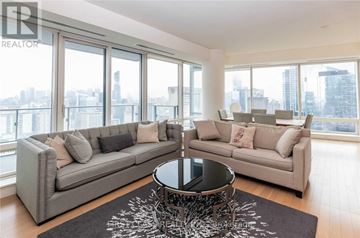 Toronto (Bay Street Corridor) condo for rent - A living room with a grey sofa and a coffee table in front of a large window.