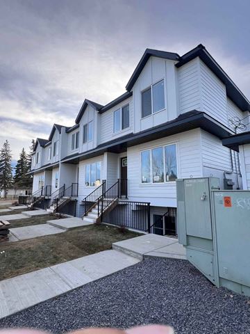 Calgary apartment for rent - A white two-story house with a black roof and a grey garage door.