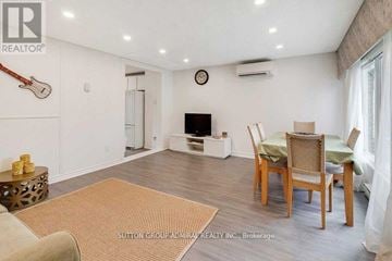 Toronto (Westminster-Branson) townhouse for rent - A living room with a brown rug, a wooden table with chairs, and a guitar hanging on the wall.