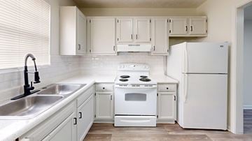 Gainseville apartment for rent - A white kitchen with a stove, sink, and refrigerator.