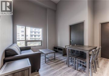 Waterloo condo for rent - A living room with a grey couch, a black leather ottoman, a wooden coffee table, a grey dining table with four chairs, and a flat screen TV mounted on the wall.