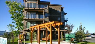 Kamloops apartment for rent - A modern multi-story building with a wooden pergola in front.