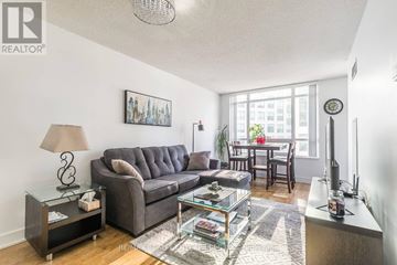 Toronto (Waterfront Communities) condo for rent - A living room with a grey couch, a glass coffee table, and a lamp on a side table.