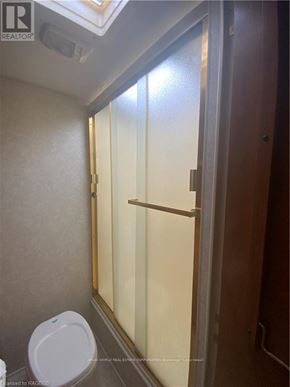 Northern Bruce Peninsula mobile home for rent - A white toilet in a small bathroom with a glass shower door.