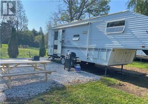Northern Bruce Peninsula mobile home for rent - A silver trailer is parked in a gravel lot with a picnic table in front of it.