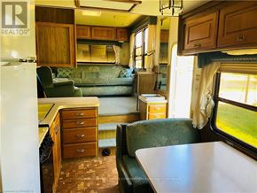 Northern Bruce Peninsula mobile home for rent - The image shows a well-furnished interior of a trailer with a green sofa, wooden cabinets, and a window with a view of grass.