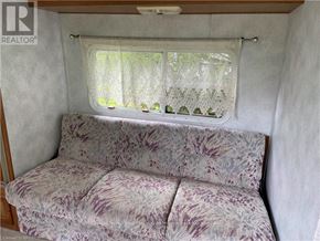 Northern Bruce Peninsula mobile home for rent - A couch with a floral pattern sits in a room with a window covered by a lace curtain.