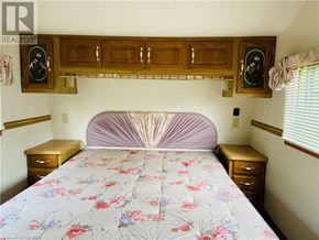 Northern Bruce Peninsula mobile home for rent - A bedroom with a bed, nightstands, and a wooden cabinet above the bed.