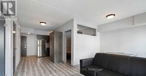 Waterloo condo for rent - A black couch is in the middle of a white room with a kitchen area in the background.