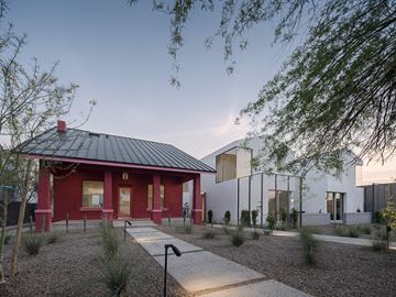 Phoenix apartment for rent - A red house with a black roof is surrounded by a white fence and has a gravel path leading to the front door.