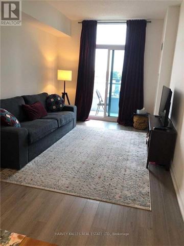 Toronto (Bayview Village) condo for rent - A living room with a grey couch, a rug, a television and a window with curtains.