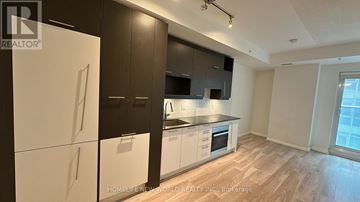Toronto (Waterfront Communities) condo for rent - A modern kitchen with white and black cabinets and a wooden floor.