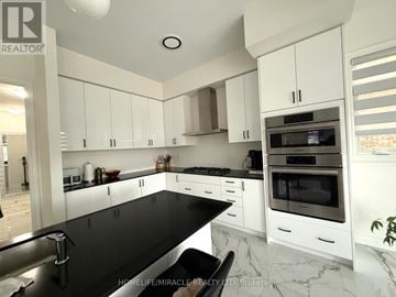 For rent in East Gwillimbury (Holland Landing) - A modern kitchen with white cabinets and black countertops.