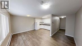 For rent in Grande Prairie - A spacious room with wooden flooring and a kitchenette in the background.