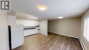 For rent in Grande Prairie - A well-lit, empty room with a white refrigerator and wooden flooring.