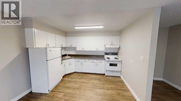 For rent in Grande Prairie - A kitchen with white appliances and cabinets in a room with wooden floors.