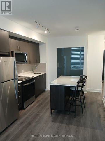 Oshawa (Windfields) condo for rent - A kitchen with a refrigerator, microwave, and a counter with a bar stool.