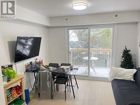 Toronto (University) house for rent - A living room with a grey couch, a television, a dining table with chairs, and a balcony with a view of trees.