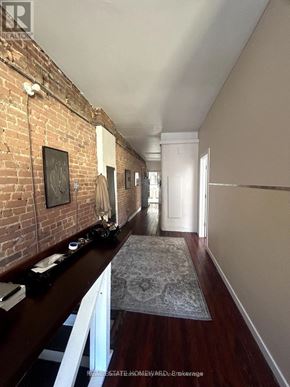 For rent in Toronto (Greenwood-Coxwell) - A long hallway with a brick wall on the left and a rug on the floor.