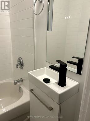 For rent in Toronto (Greenwood-Coxwell) - A white bathroom sink with a black faucet and a white bathtub.