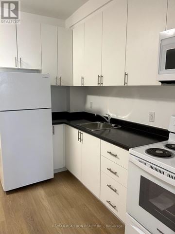 Toronto (Greenwood-Coxwell) other for rent - A white refrigerator stands in a kitchen with white cabinets and a black countertop.