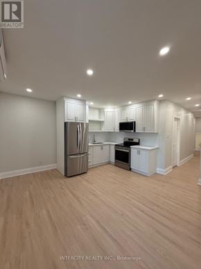 Toronto (Annex) house for rent - A well-lit, empty kitchen with white cabinets and a wooden floor.