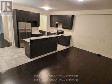 Brampton (Northwest Brampton) townhouse for rent - A kitchen with dark wood floors and cabinets, a refrigerator, a sink, and a stove top oven.