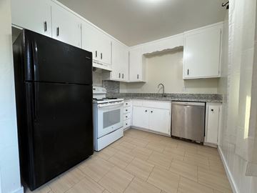 Oakland apartment for rent - A black refrigerator stands in a kitchen with white cabinets and a granite countertop.